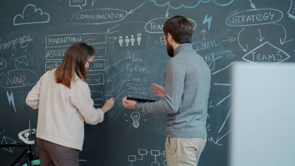 Two people writing on a blackboard