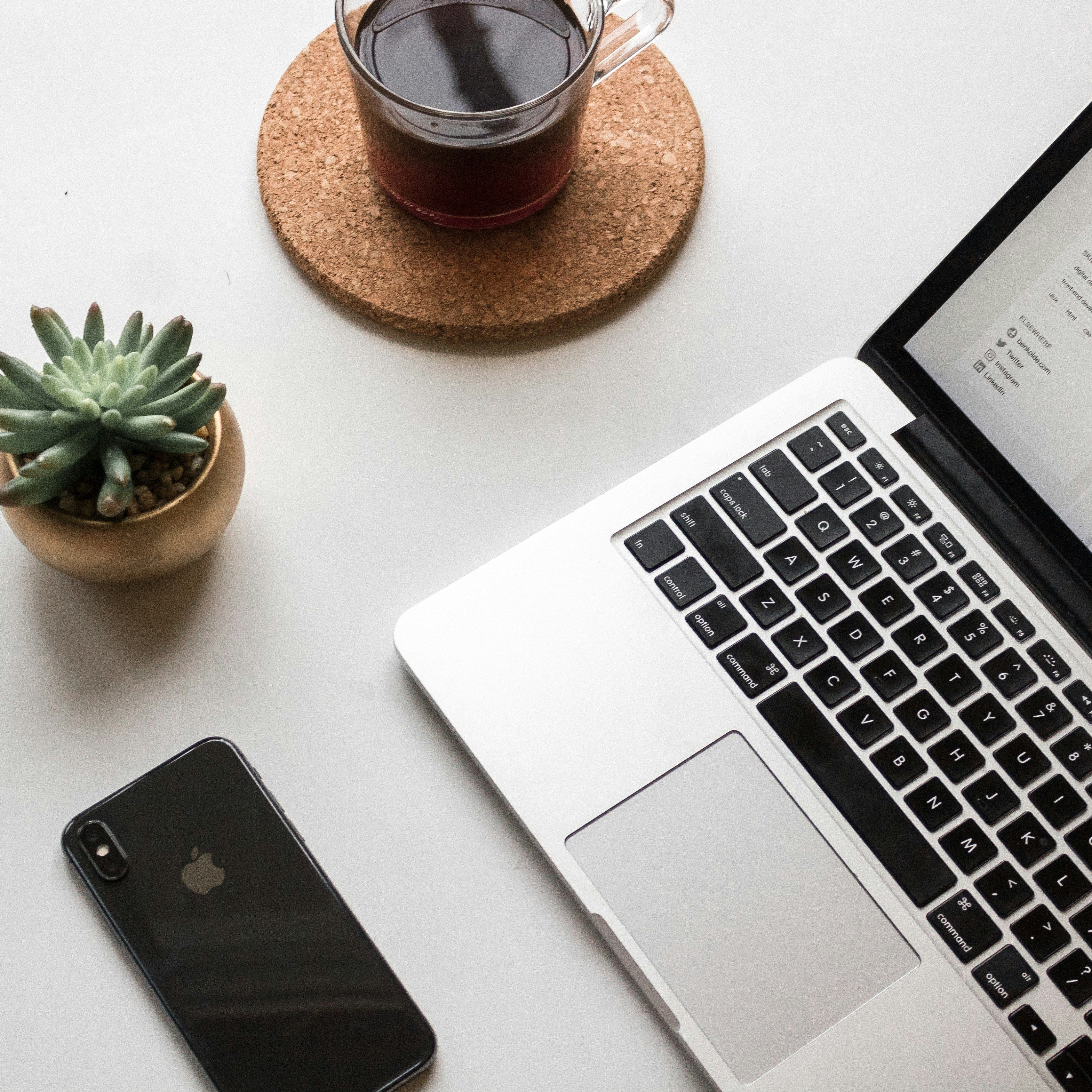 A computer, mobile phone, cup of coffee, and plant neatly organized on a table